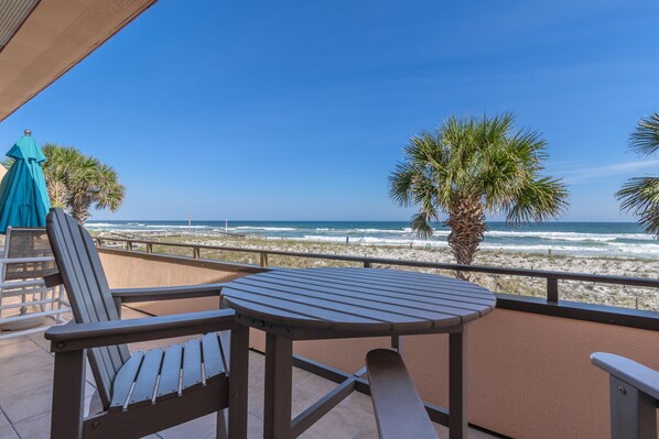Ein Balkon mit Tisch und Stühlen mit Blick auf einen Strand mit Palmen und Wellen.