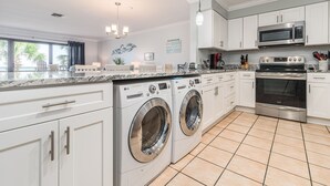 A modern kitchen with stainless steel appliances, white cabinetry, and a large window overlooking a palm tree.