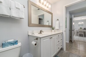 Ein Badezimmer mit Waschbecken, Spiegel und Toilette. Handtücher hängen an der Wand, und neben der Toilette steht ein Mülleimer.