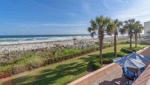 A beach view with a patio area featuring a blue umbrella and lounge chairs.