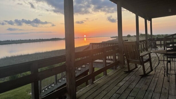 Una terraza de madera con vista a un atardecer sobre una masa de agua.