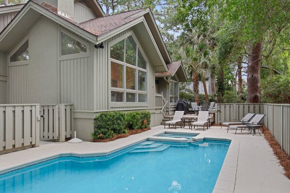 A residential property with a swimming pool, outdoor seating, and a covered patio area.