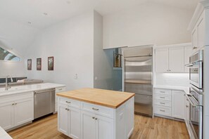 A modern kitchen with white cabinetry, a wooden island, stainless steel appliances, and a window providing natural light. - Direct Beach Path & Pool Near The Salty Dog Cafe (Hilton Head Island)