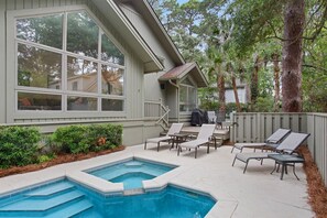 A backyard with a swimming pool, lounge chairs, and a covered patio area.