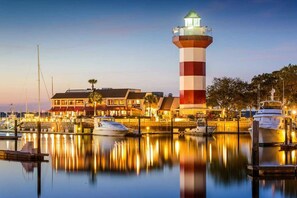 A waterfront property with a prominent lighthouse, marina with boats, and a building with a red and white facade. - Direct Beach Path & Pool Near The Salty Dog Cafe (Hilton Head Island)