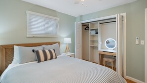 A bedroom with a bed, bedside table, lamp, and a walk-in closet with a mirror and shelves.