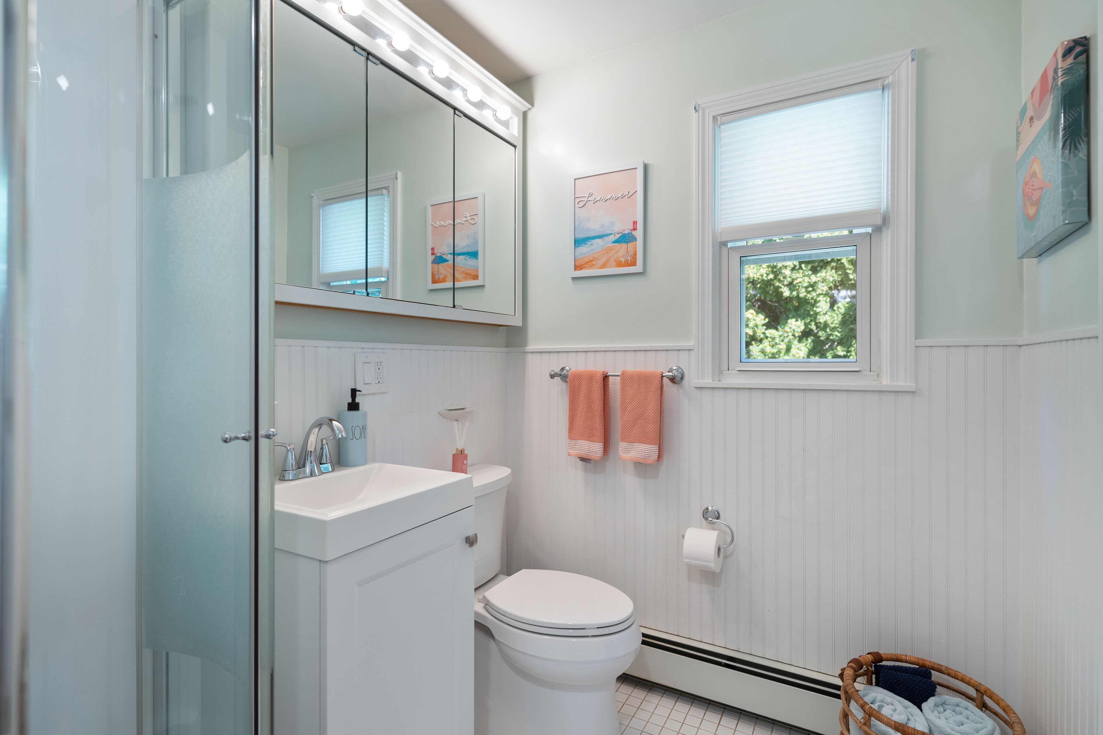 Un bagno con cabina doccia in vetro, un lavandino bianco, un water e una finestra con vista sugli alberi.