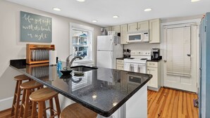 Una cocina moderna con una isla central, taburetes de bar, refrigerador, microondas, horno y una pizarra con una frase motivadora.