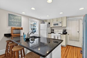 A modern kitchen with a central island, bar stools, a refrigerator, microwave, oven, and a chalkboard with a motivational quote.