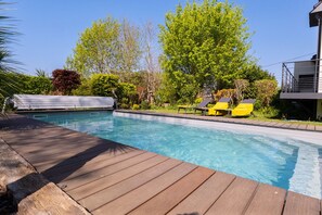 Une piscine dotée d’une terrasse en bois, entourée d’arbres et bordée d’un bâtiment avec un balcon.