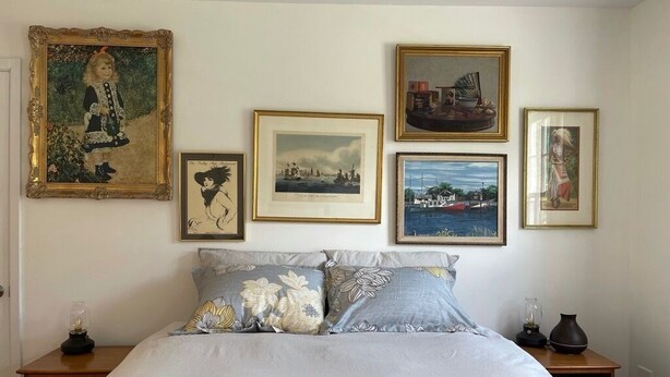 Un dormitorio con cama, almohadas y una mesita de noche. En la pared hay cuadros enmarcados.