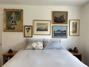 Un dormitorio con cama, almohadas y una mesita de noche. En la pared hay cuadros enmarcados.