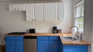 Una cocina con armarios azules, encimera de madera, lavavajillas, estufa y ventana con vistas al verdor.
