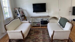 Una sala de estar con dos sofás blancos, un televisor, una estantería y una puerta.