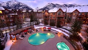 A resort with a large outdoor pool, multiple buildings, and snow-covered mountains in the background. - Stoneridge 2 BDR - Sleeps 8★ Hot Tub/ Pool/Sauna/Gym ★Mountain Views ★1100 SQF (Canmore)