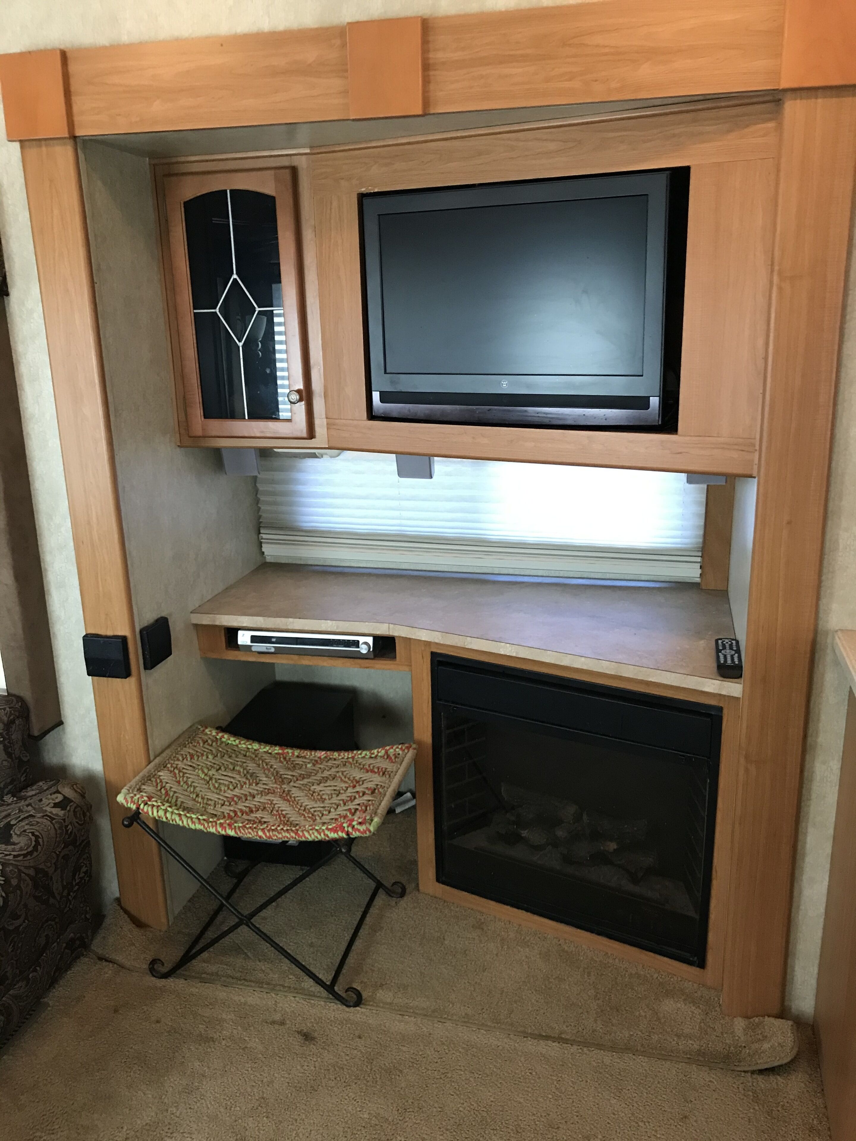 A compact RV interior with a television mounted on a wooden cabinet, a small kitchenette area, and a foldable table.