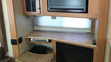 A compact RV interior with a television mounted on a wooden cabinet, a small kitchenette area, and a foldable table.