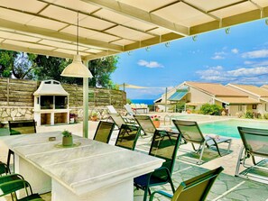 Ein überdachter Außenbereich mit Pool, Liegestühlen, einem Tisch und einem Grill.