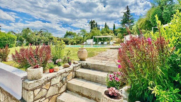 Un jardí amb escales de pedra que condueixen a una zona de piscina, envoltat de vegetació exuberant i un cel serè.