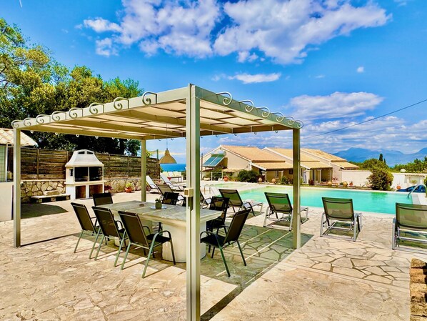 Ein überdachter Außenbereich mit Pool, Liegestühlen und Grill.