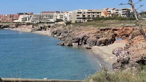 Une zone côtière caractérisée par une côte rocheuse, une plage de sable et une rangée d’immeubles à plusieurs étages en arrière-plan.