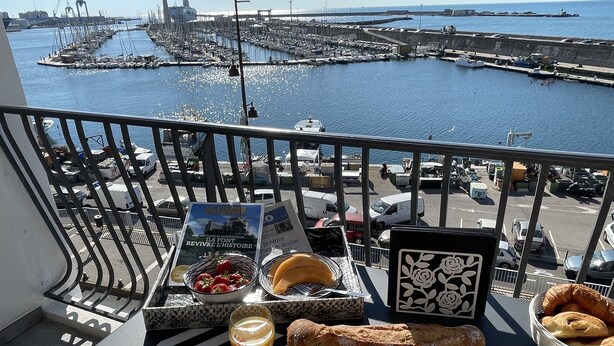 Un balcon avec une table dressée pour le petit-déjeuner, donnant sur une marina avec des bateaux et une jetée.