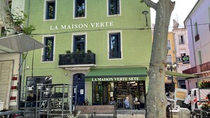Un bâtiment vert portant l’enseigne « LA MAISON VERTE » et une plus petite enseigne « LA MAISON VERTE SÈTE », indiquant qu’il s’agit d’un café ou d’un restaurant.