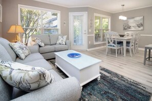 Un salon comprenant un canapé, une table basse, une table à manger avec des chaises, et donnant sur l’extérieur.