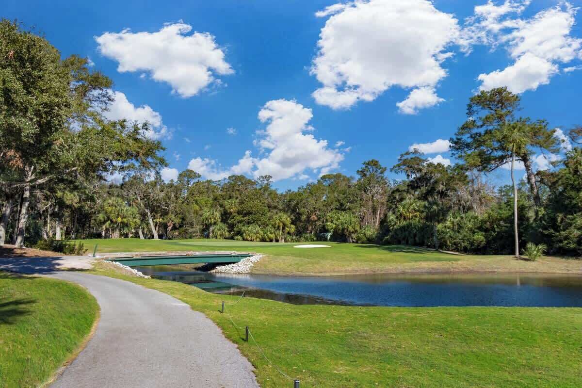 Un campo da golf con uno stagno, alberi e cielo sereno.