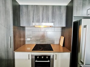 Compact kitchen with stove, oven, and microwave, featuring a textured wood cabinetry.