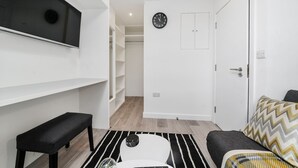 A modern living room with a black bench, a white coffee table, a patterned rug, and a sofa with a chevron-patterned throw. - Cosy Apartment in the Heart of the City (London)