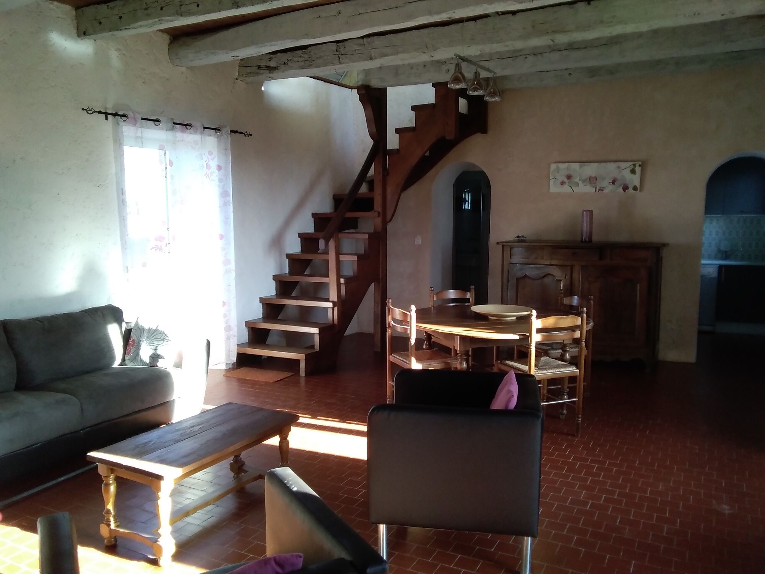 Een woonkamer met een bank, een houten tafel, een stoel, een trap en een eethoek met een tafel en stoelen.