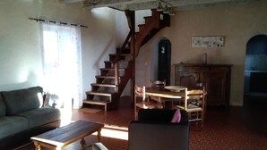 Una sala de estar con un sofá, una mesa de madera, una silla, una escalera y un comedor con una mesa y sillas.