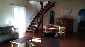 Een woonkamer met een bank, een houten tafel, een stoel, een trap en een eethoek met een tafel en stoelen.