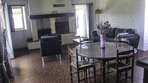 Un interior rústico con vigas de madera a la vista, suelo de ladrillo, una mesa redonda con sillas, un sofá y una chimenea.