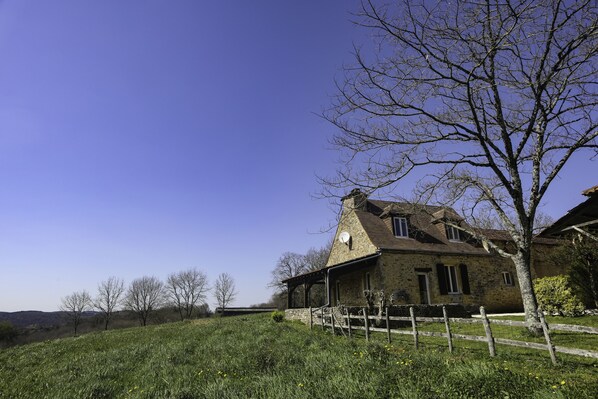 A stone house with a sloped roof, a wooden fence, and a clear blue sky.