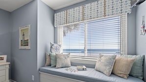 Una habitación con asiento junto a la ventana, decoración náutica, un reloj y un cuadro en la pared.