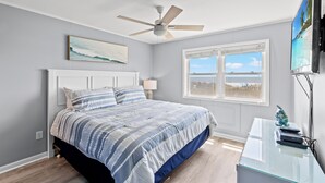 A bedroom with a bed, a ceiling fan, a window with a view, and a desk with a fish sculpture. - Ocean Pier I 107-2BR/2BA Oceanfront Condo in Windy Hill (North Myrtle Beach)