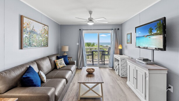 A living room with a sofa, coffee table, and TV. There is a balcony with a view of the ocean. - Ocean Pier I 107-2BR/2BA Oceanfront Condo in Windy Hill (North Myrtle Beach)