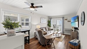 A modern living room with a ceiling fan, a sofa, a coffee table, and a TV on the wall.