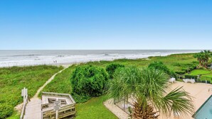 A beach view with a wooden deck, a pool, and a path leading to the beach.