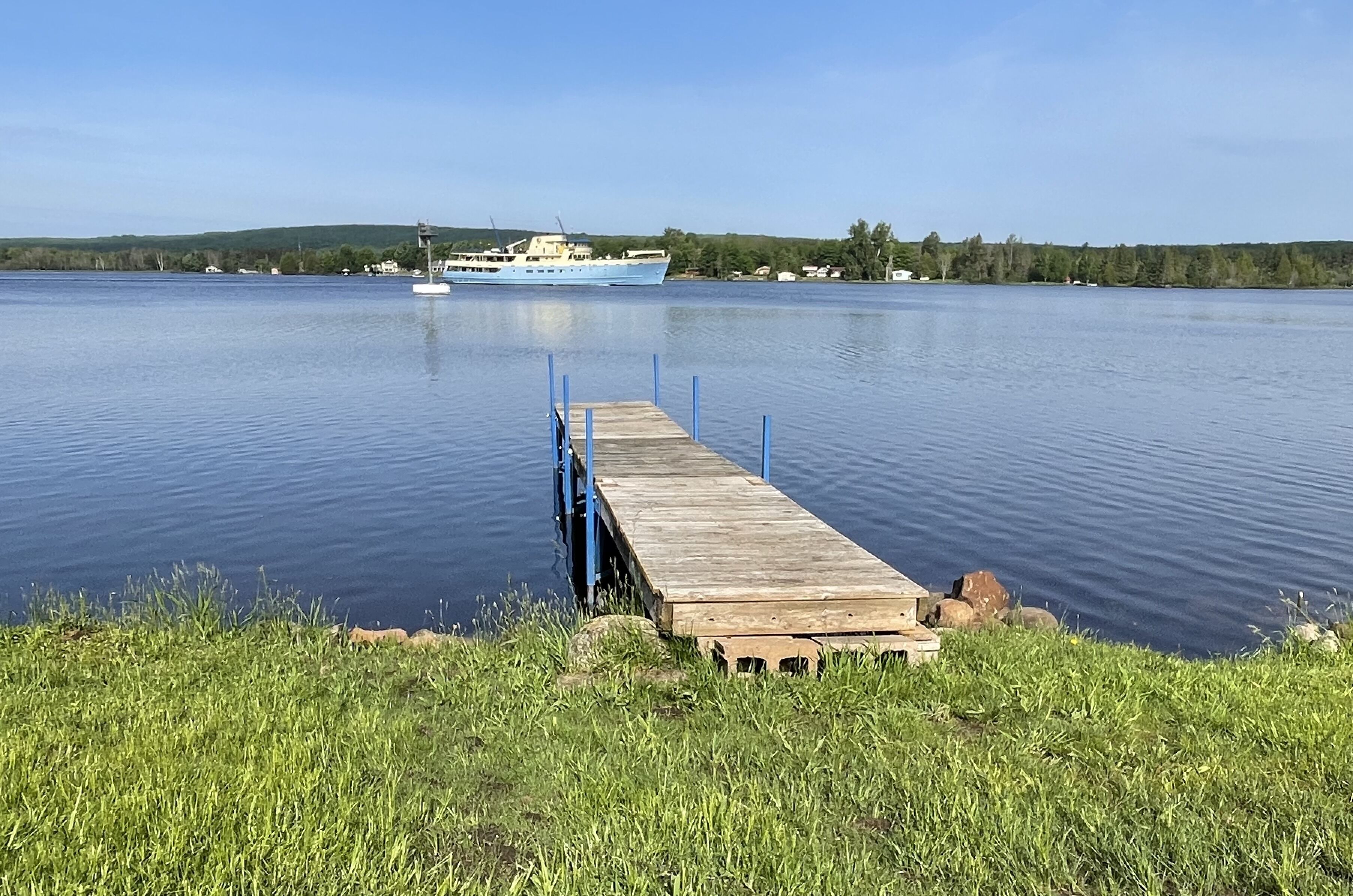 A wooden pier extending into calm water with a large boat docked in the background.