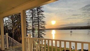A wooden deck with white railings overlooking a lake with a sunset.