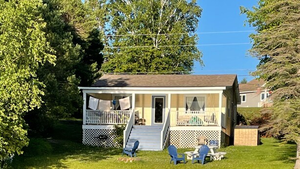 A lakeside house with a porch, two blue chairs, and a small table.