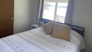 A bedroom with a bed, a nightstand, a window with curtains, and a view of a body of water.