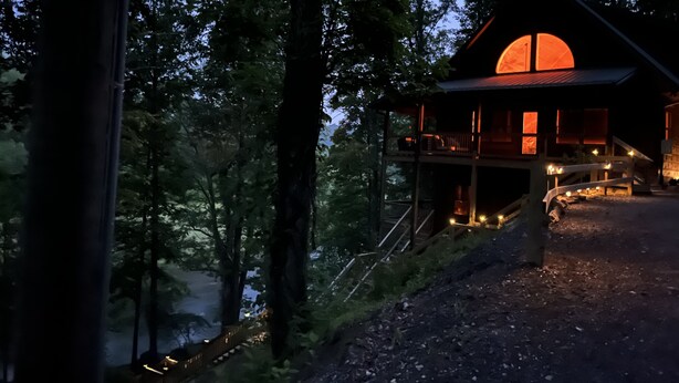 Eine Hütte mit einem großen, runden Fenster, umgeben von Bäumen, und über eine Holztreppe erreichbar.