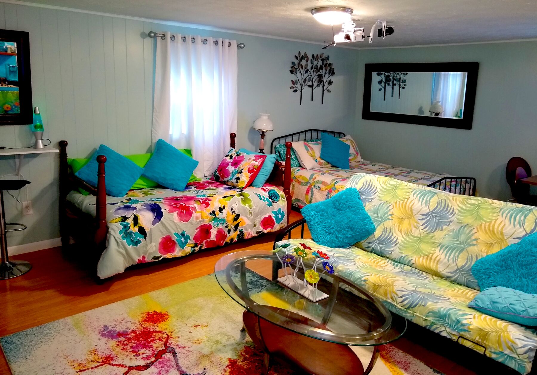 A cozy bedroom with two beds, a glass coffee table, and a colorful rug.