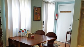 Ein Essbereich mit einem Holztisch, sechs Stühlen, einer kleinen Zimmerpflanze und einer gerahmten Speisekarte an der Wand.