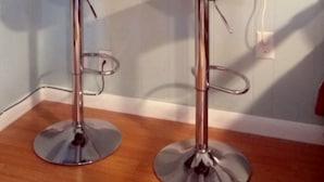 Eine Küche mit zwei Barhocker, einem Spiegel über einem weißen Regal und einer Vase mit roten Blumen.
