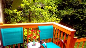 Eine Holzterrasse mit zwei Stühlen und einem kleinen runden Tisch, umgeben von üppigem Grün.